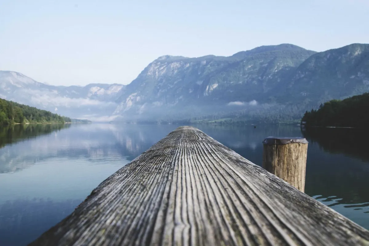 A wooden jetty reaching into a still mountain lake at dawn